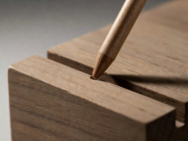 A wooden pin entering a test slot with a small visible clearance at its upper edge